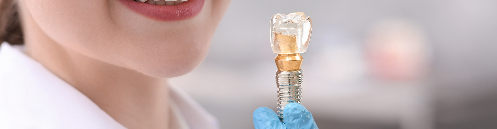 smiling woman's gloved hand holding model of an implant